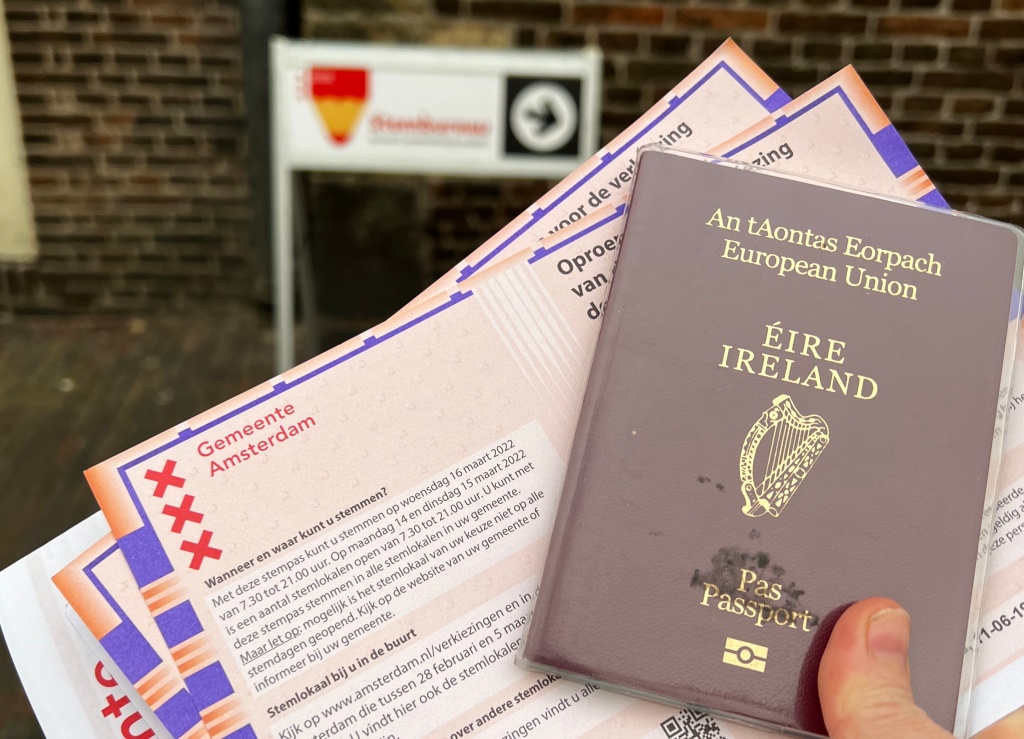 A hand holds an Irish passport and Dutch voting papers